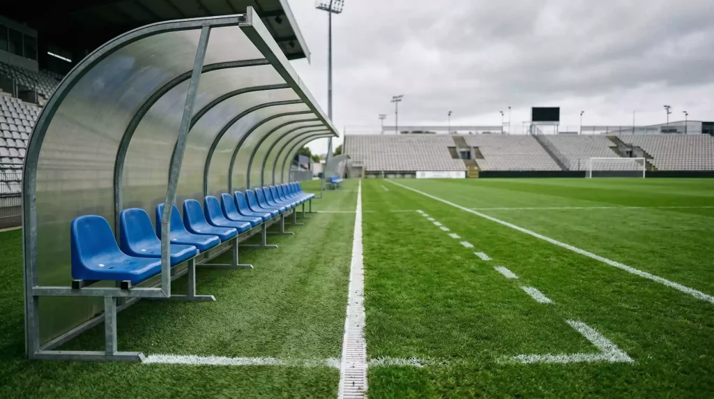 Banquillo vacío de un estadio de fútbol italiano con el campo de césped en perspectiva
