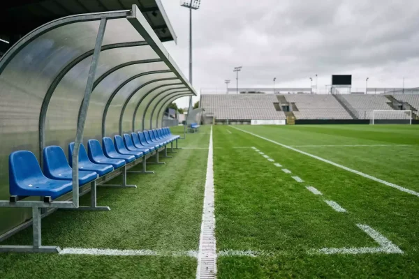 Banquillo vacío de un estadio de fútbol italiano con el campo de césped en perspectiva