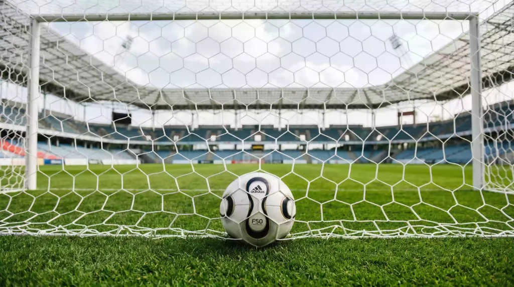 Balón de fútbol dentro de la red de una portería en un estadio italiano con gradas al fondo